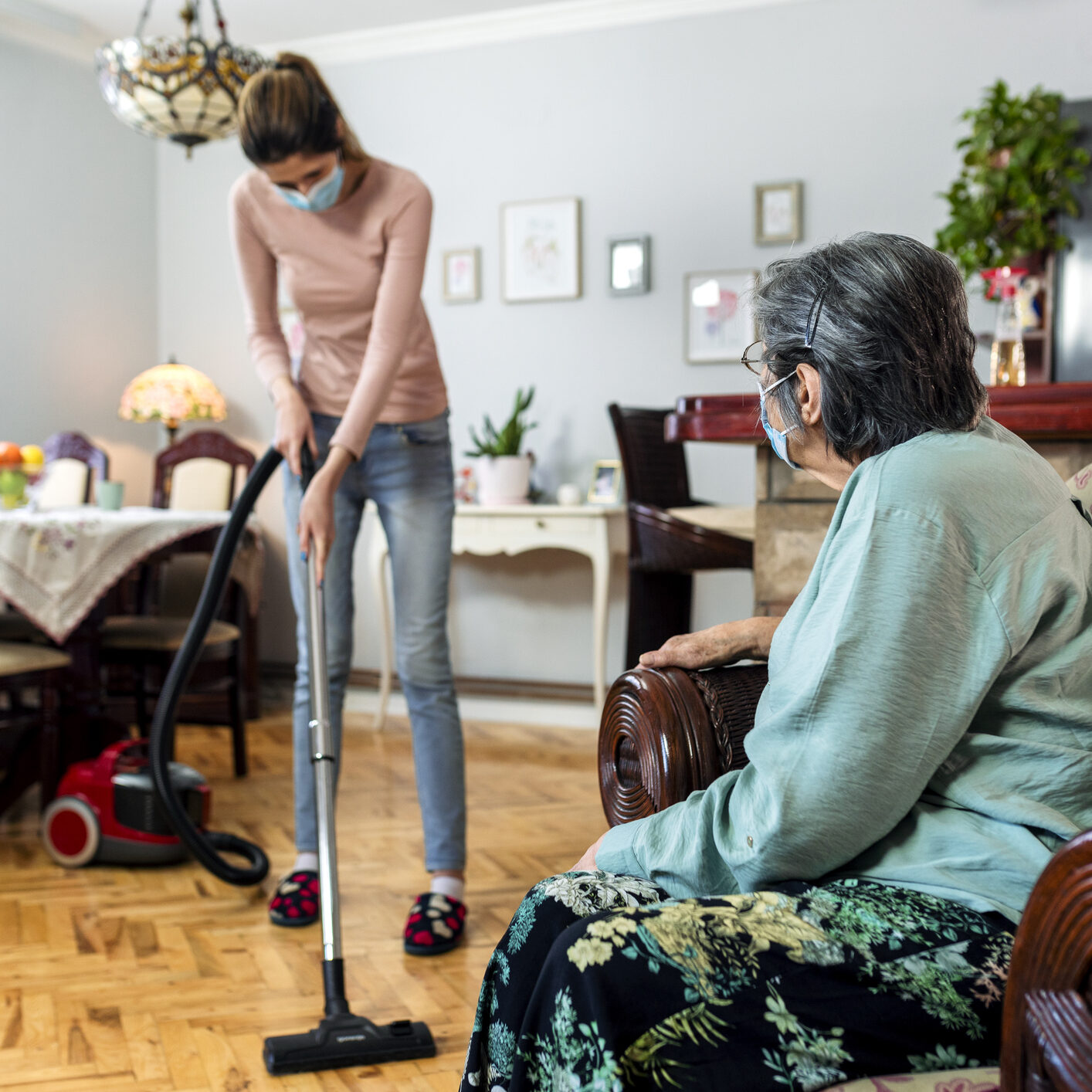 Young woman vacuuming near elderly lady
