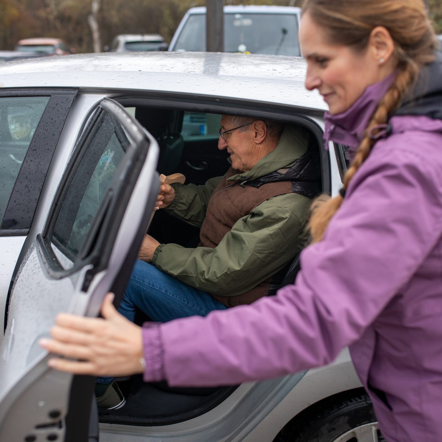 Woman helps elderly man into car